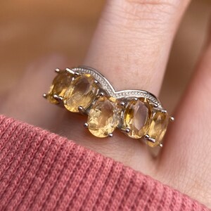 May include: A silver ring with a V-shaped band and five oval-shaped yellow gemstones.