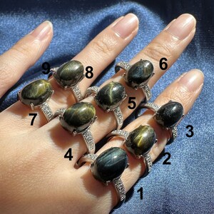 K&ouml;nnte beinhalten: Neun Silberringe mit ovalen, blau-gr&uuml;nen Tigeraugen-Edelsteinen. Die Ringe sind von 1 bis 9 nummeriert.
