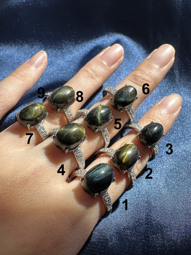 K&ouml;nnte beinhalten: Neun Silberringe mit ovalen, blau-gr&uuml;nen Tigeraugen-Edelsteinen. Die Ringe sind von 1 bis 9 nummeriert.