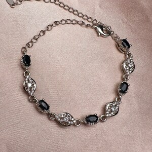 May include: A silver bracelet with a delicate chain and oval-shaped black stones set in a silver frame with smaller white stones.