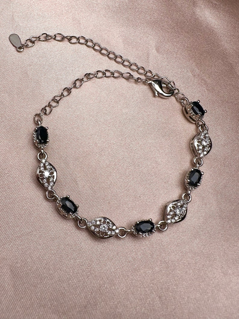 May include: A silver bracelet with a delicate chain and oval-shaped black stones set in a silver frame with smaller white stones.