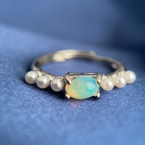 May include: A silver ring featuring a light blue opal gemstone and five small white pearls on the band.