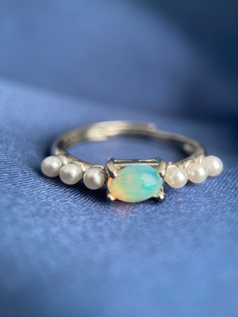 May include: A silver ring featuring a light blue opal gemstone and five small white pearls on the band.