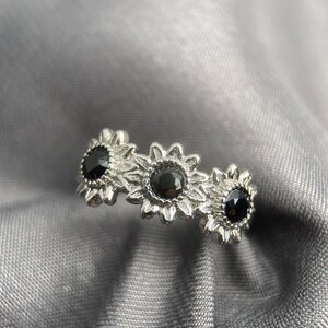 May include: A silver ring with three black gemstones set in a sunflower design.