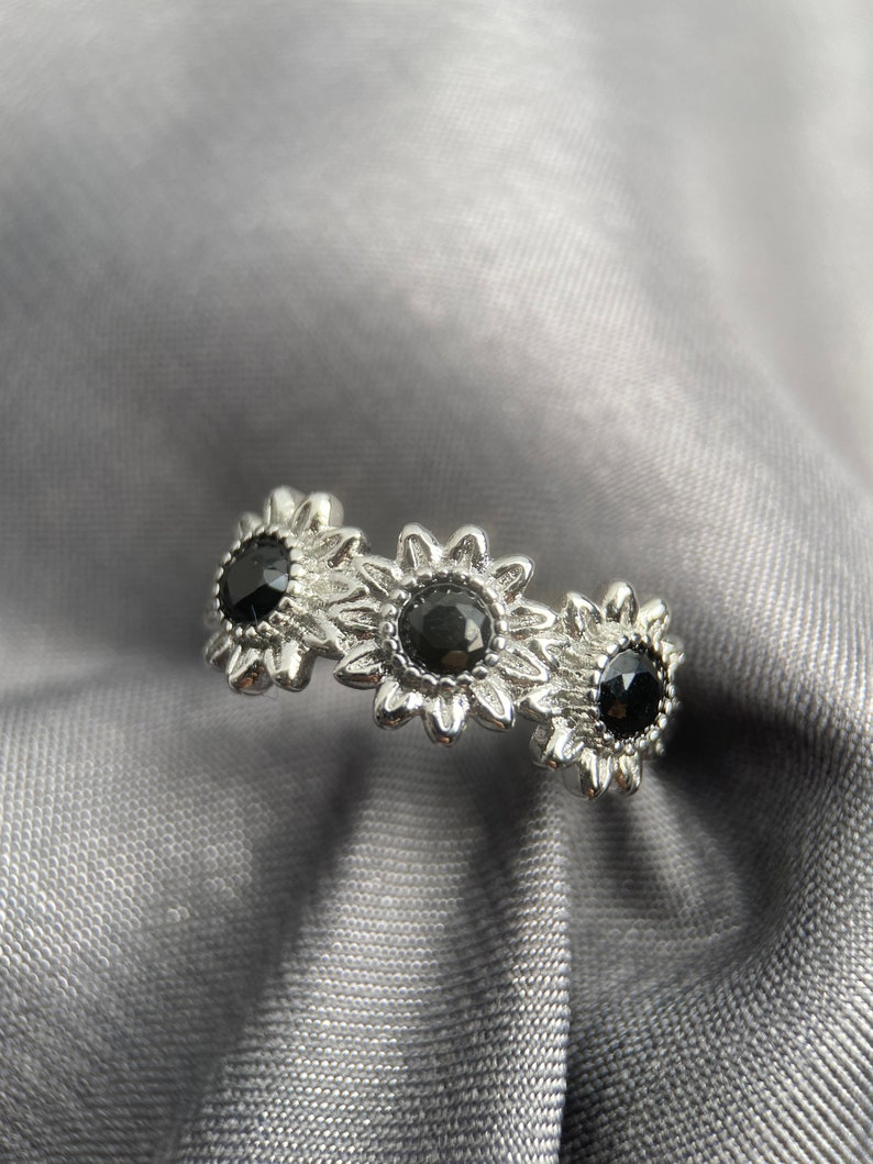 May include: A silver ring with three black gemstones set in a sunflower design.
