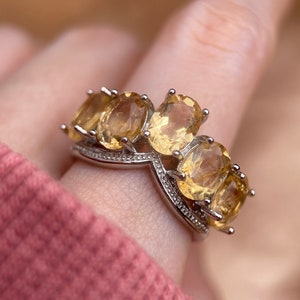 May include: A silver ring with a V-shaped band and four oval-shaped yellow gemstones.