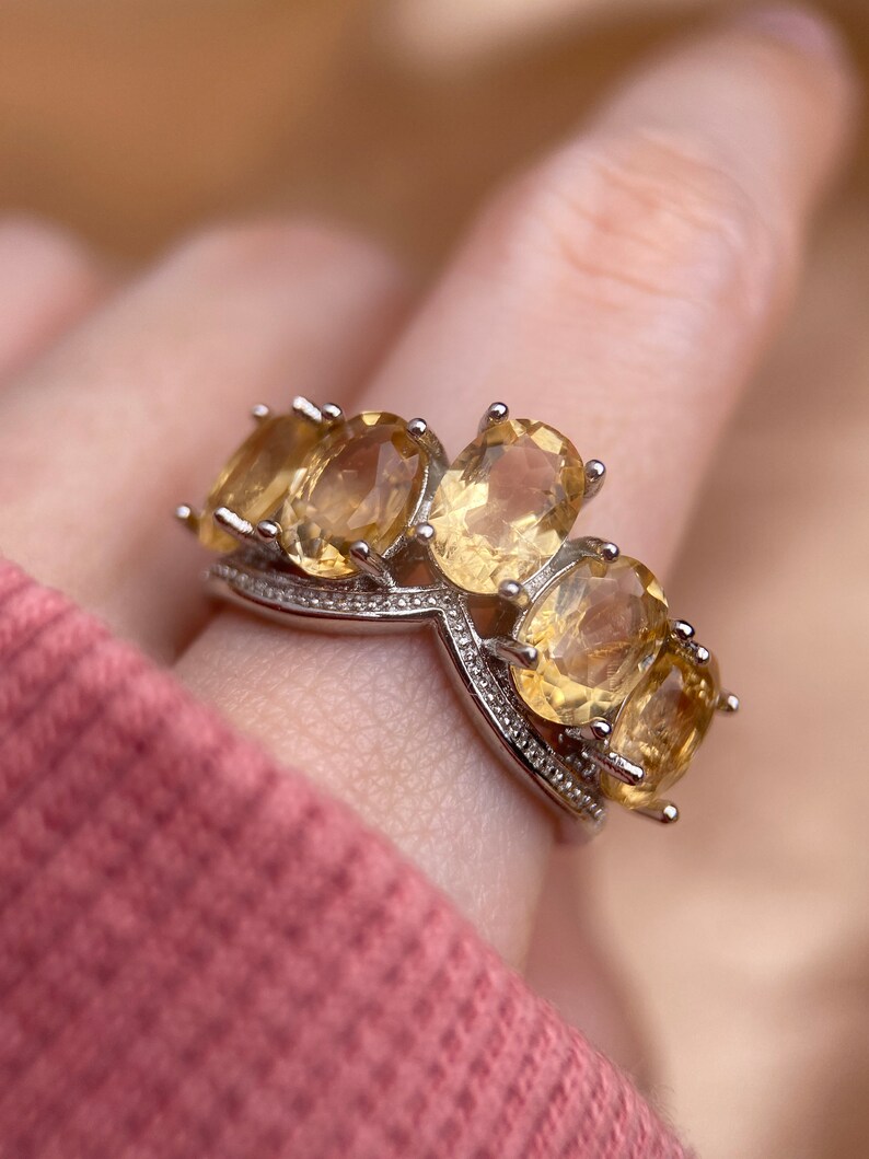 May include: A silver ring with a V-shaped band and four oval-shaped yellow gemstones.