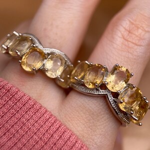 May include: A silver ring with a row of oval-shaped, light yellow gemstones. The ring has a delicate, twisted band.