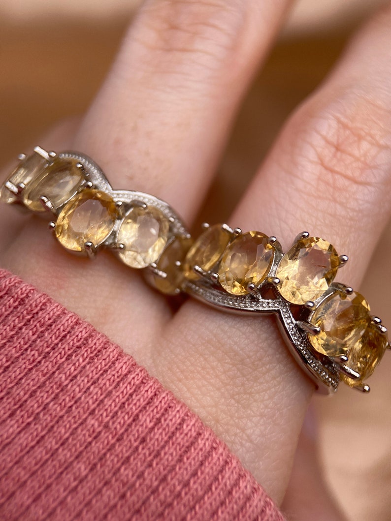 May include: A silver ring with a row of oval-shaped, light yellow gemstones. The ring has a delicate, twisted band.