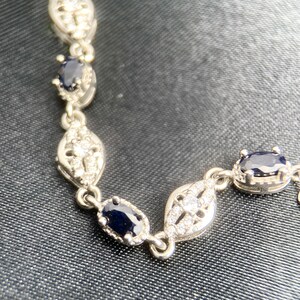 May include: A silver bracelet with a delicate design featuring oval-shaped blue gemstones and smaller clear gemstones.