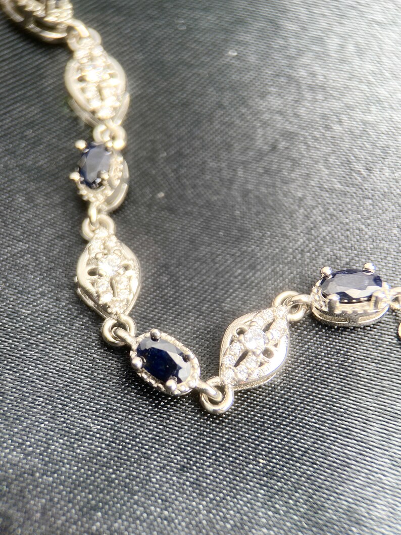 May include: A silver bracelet with a delicate design featuring oval-shaped blue gemstones and smaller clear gemstones.