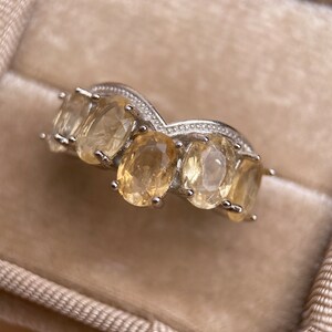 May include: A silver ring with five oval-shaped, light yellow gemstones set in a curved band.