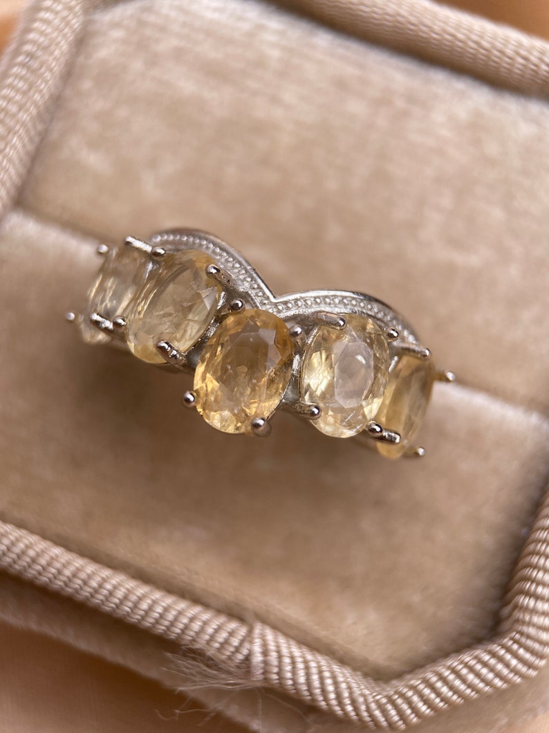 May include: A silver ring with five oval-shaped, light yellow gemstones set in a curved band.