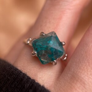 May include: A silver ring with a faceted, green gemstone. The gemstone has a unique, marbled pattern.