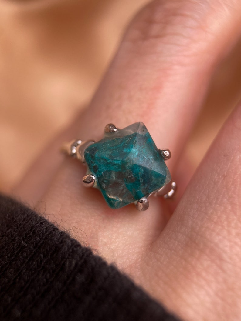 May include: A silver ring with a faceted, green gemstone. The gemstone has a unique, marbled pattern.