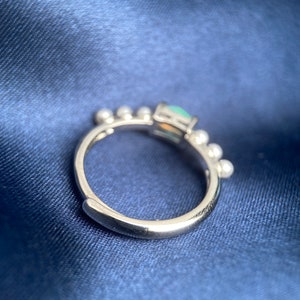 May include: A silver ring featuring a green gemstone and small white beads around the band.