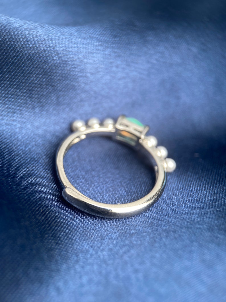 May include: A silver ring featuring a green gemstone and small white beads around the band.