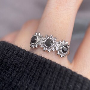 May include: A silver ring with three black sunflower designs. Each sunflower has a black gemstone in the center.