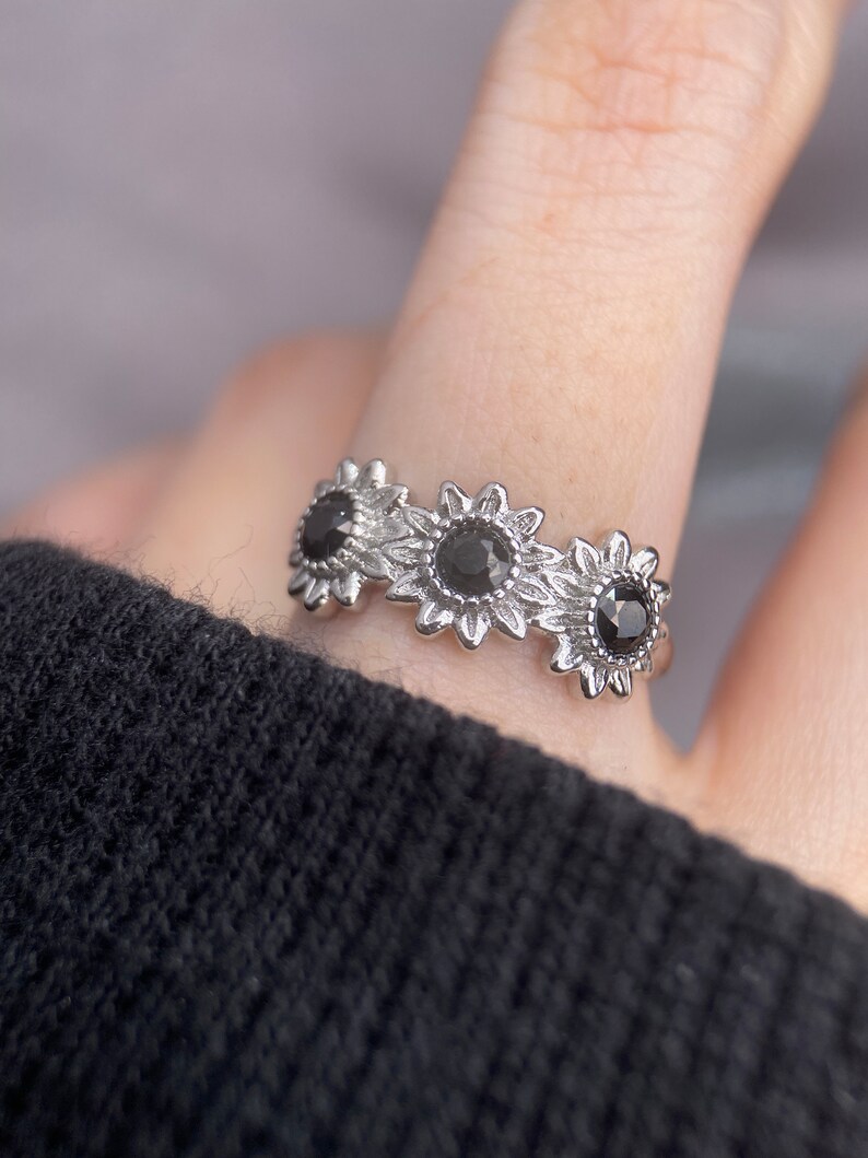 May include: A silver ring with three black sunflower designs. Each sunflower has a black gemstone in the center.