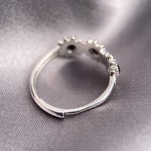 May include: Silver ring with a delicate design of small, round stones set in a floral pattern.