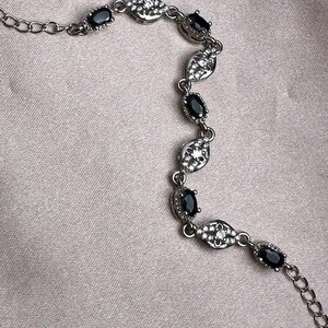 May include: A silver bracelet with a delicate chain and black oval-shaped stones set in a silver leaf design.