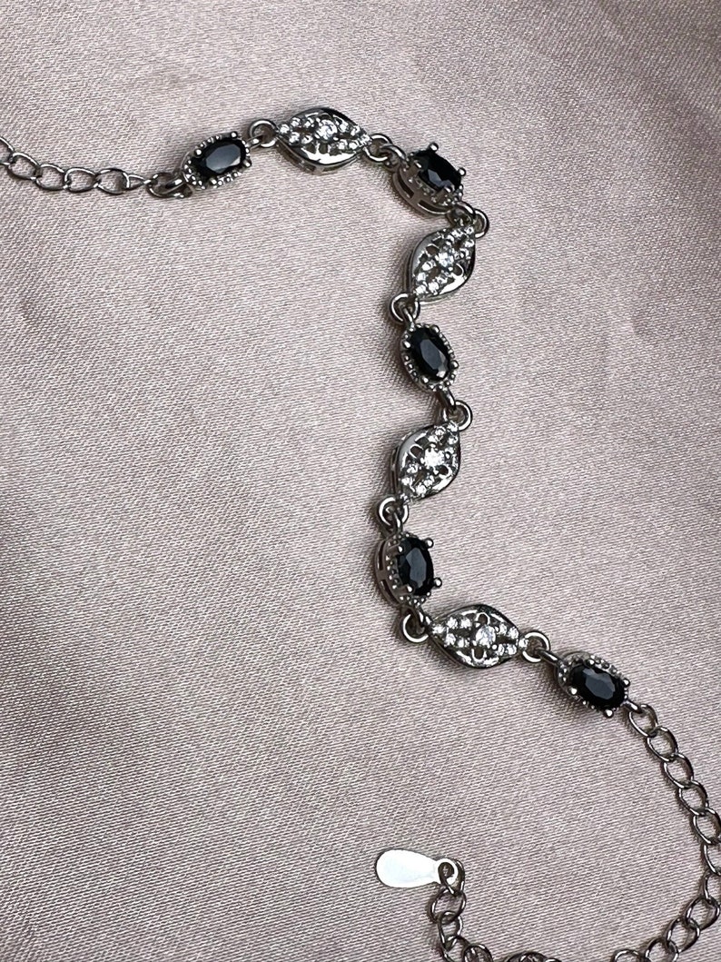 May include: A silver bracelet with a delicate chain and black oval-shaped stones set in a silver leaf design.