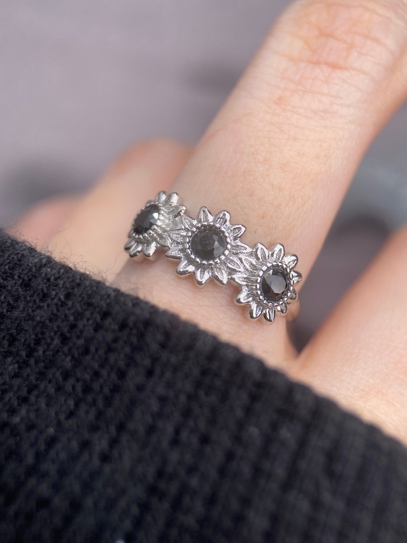 May include: Silver ring with three black sunflower designs. Each sunflower has a black gemstone in the center.