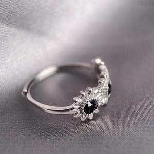 May include: A silver ring with three black gemstones set in a flower design.