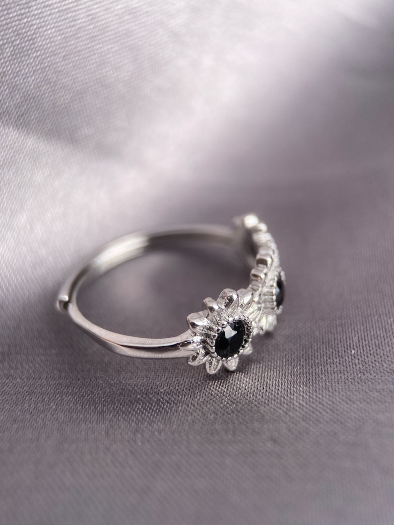 May include: A silver ring with three black gemstones set in a flower design.