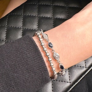May include: Two silver bracelets with black and white stones. The bracelets are stacked on a person's wrist.