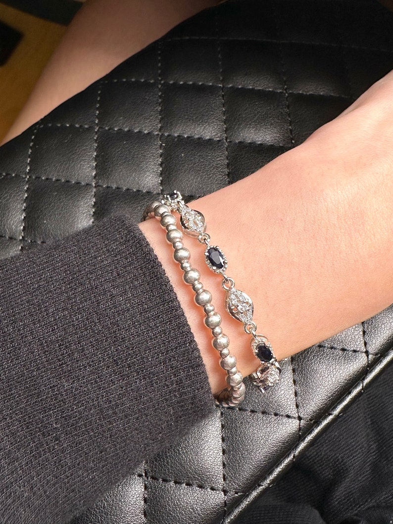 May include: Two silver bracelets with black and white stones. The bracelets are stacked on a person's wrist.
