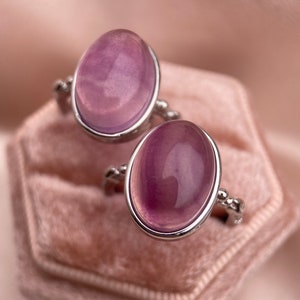 May include: Two silver rings with oval-shaped purple gemstones set in a velvet ring box.