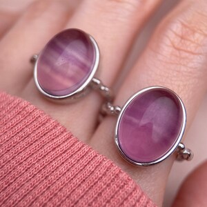 May include: Two silver rings with oval-shaped purple stones. The rings are on a finger.