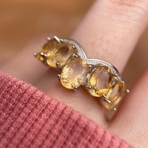 May include: A silver ring with five oval-shaped yellow gemstones set in a V-shaped band.