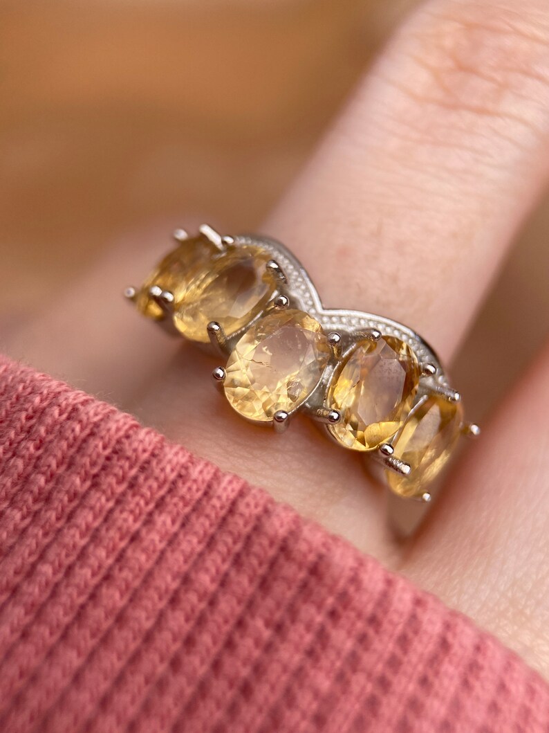May include: A silver ring with five oval-shaped yellow gemstones set in a V-shaped band.