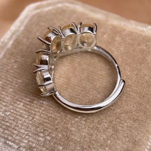 May include: A silver ring with four clear oval-shaped stones set in a curved band.