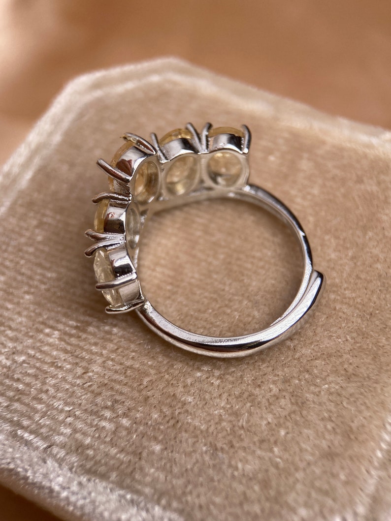 May include: A silver ring with four clear oval-shaped stones set in a curved band.