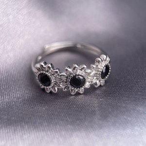 May include: A silver ring with three black gemstones set in a sunflower design.