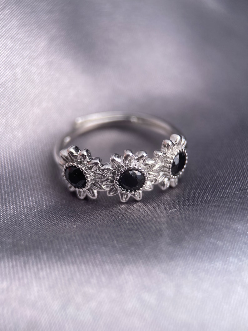 May include: A silver ring with three black gemstones set in a sunflower design.