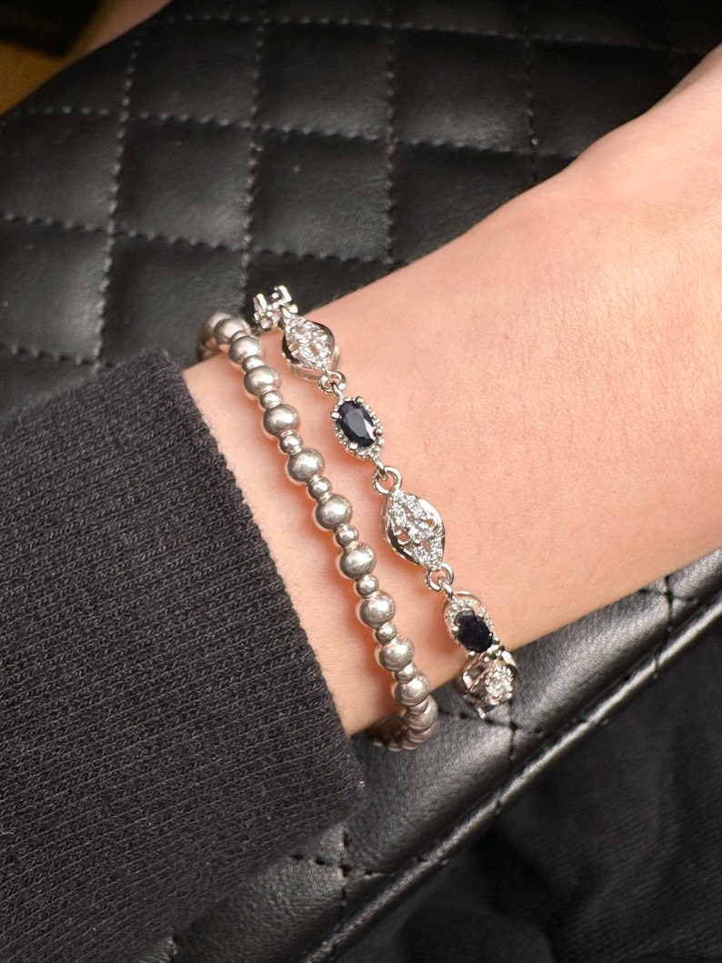 May include: Two silver bracelets with black gemstones and clear crystals. The bracelets are stacked on a person's wrist.