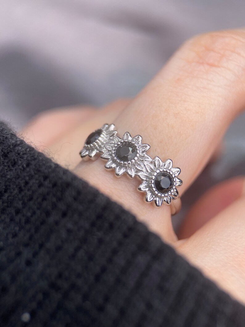 May include: A silver ring with three black gemstones set in sunflower designs.