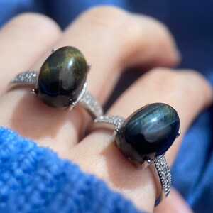 K&ouml;nnte beinhalten: Zwei Silberringe mit ovalen schwarzen und gr&uuml;nen Edelsteinen. Die Ringe sind mit kleinen klaren Steinen um die Edelsteine besetzt.
