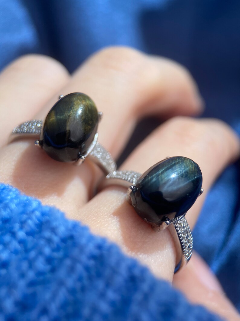 K&ouml;nnte beinhalten: Zwei Silberringe mit ovalen schwarzen und gr&uuml;nen Edelsteinen. Die Ringe sind mit kleinen klaren Steinen um die Edelsteine besetzt.