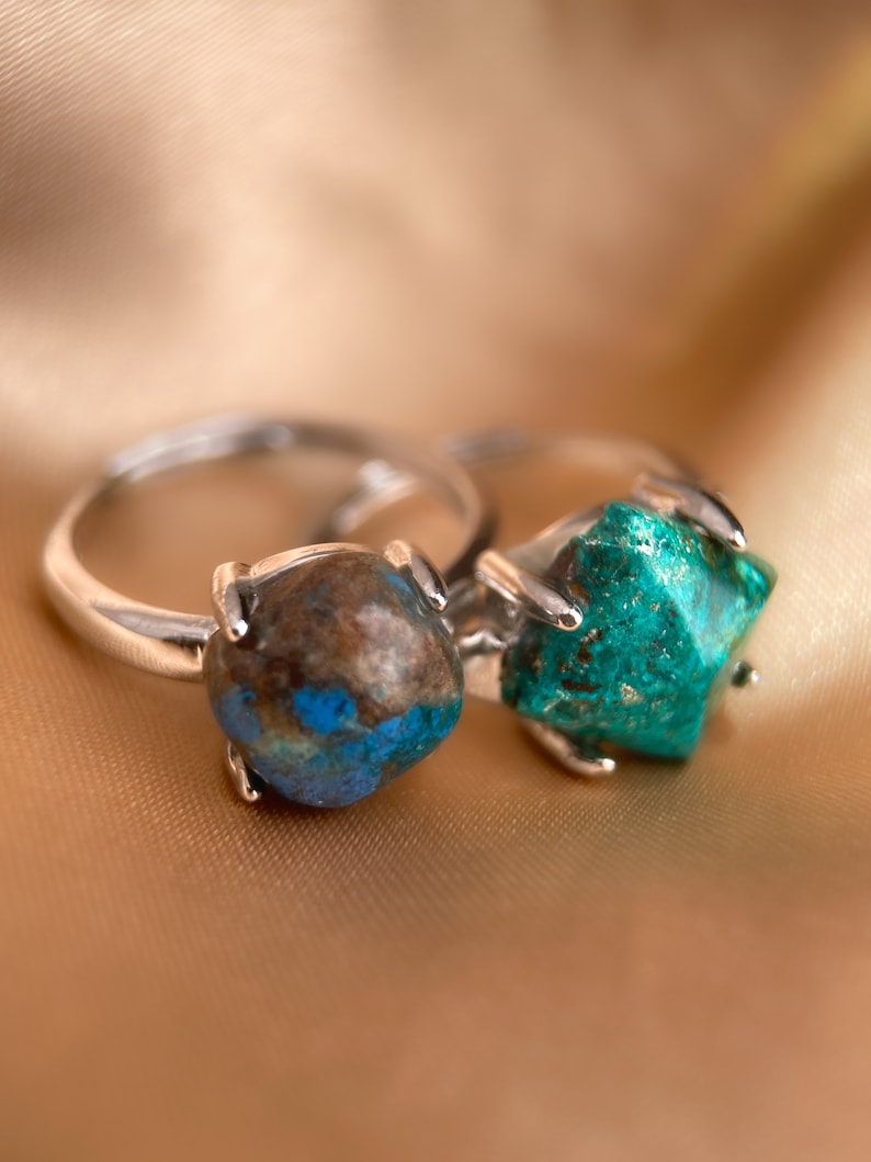 May include: Two silver rings with green and brown gemstone settings. The rings are on a gold fabric background.