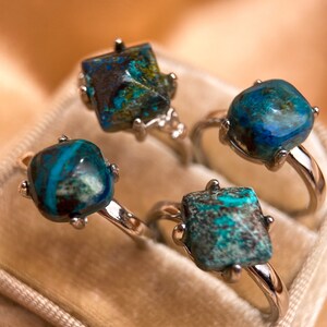 May include: Four silver rings with turquoise blue gemstone settings. The rings are displayed in a velvet ring box.