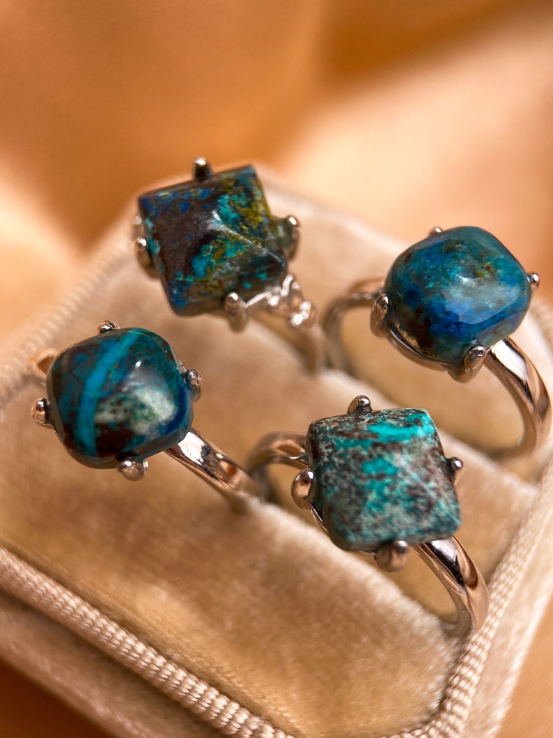 May include: Four silver rings with turquoise blue gemstone settings. The rings are displayed in a velvet ring box.