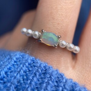 May include: A silver ring featuring a white opal gemstone and a row of white pearls.