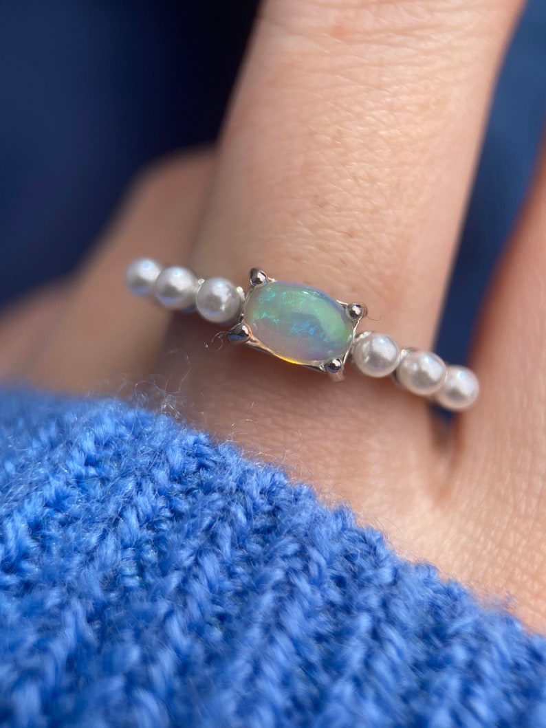 May include: A silver ring featuring a white opal gemstone and a row of white pearls.