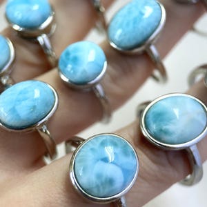 以下が含まれることがあります： 大きな水色の宝石が特徴のシルバーリングのコレクション。宝石は雲のような大理石模様です。リングはクローズアップで表示され、磨かれたシルバーバンドと石のユニークな色のバリエーションが強調されています。