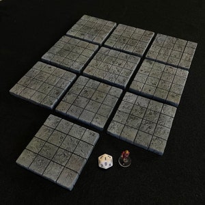 May include: Ten gray, square, tile-like pieces with a grid pattern. The tiles are arranged in a staggered pattern. A single white die with black numbers is in the lower right corner of the image.